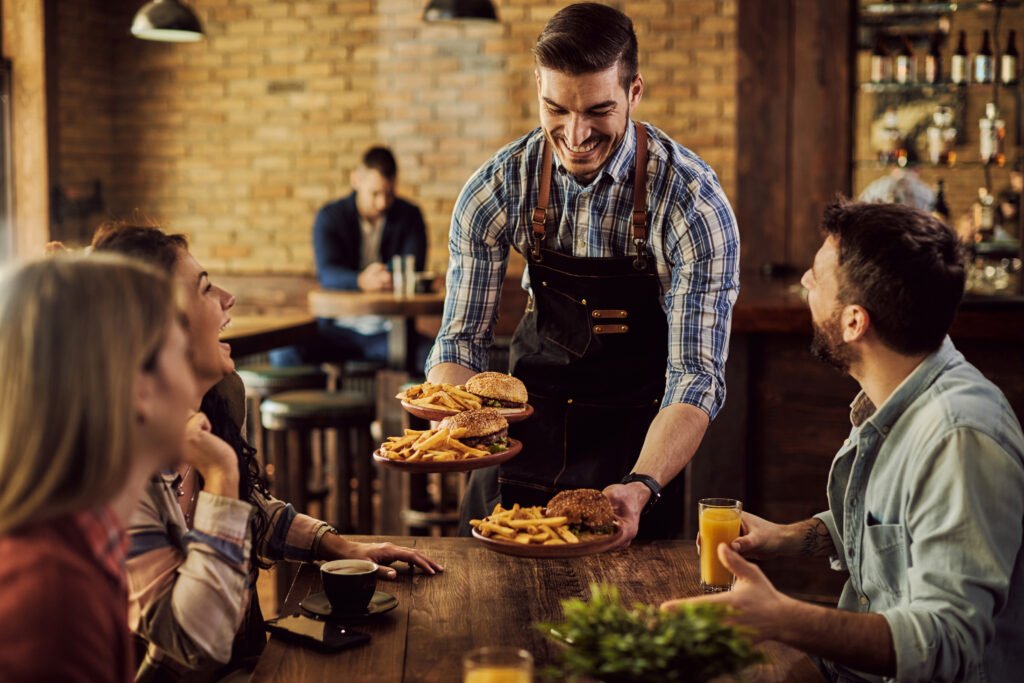 happy waiter serving food to group of cheerful friends in a pub.